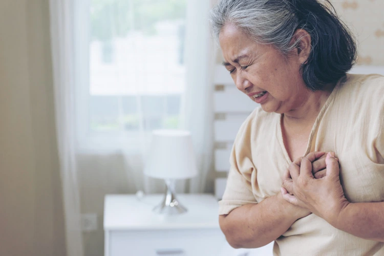 Elderly woman placing her hands on her chest area after feeling chest pains.