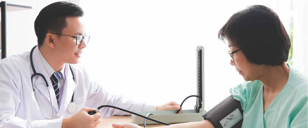 Doctor taking blood pressure of female patient who is undergoing health screening at clinic.